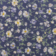 a close-up view of a fabric with a floral pattern. The fabric has a dark blue background with white and yellow flowers and leaves scattered across it. The flowers appear to be in full bloom, creating a vibrant and lively visual effect. The pattern repeats itself throughout the fabric, creating a sense of continuity and rhythm.