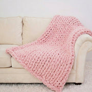 A cozy pink knitted blanket is draped over a beige couch, creating a warm and inviting atmosphere in the room.