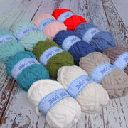 A collection of various yarn balls in different colors, including blue, green, red, and white, arranged on a wooden surface.