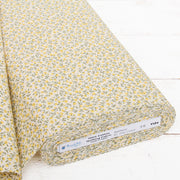 A roll of fabric with a yellow and green floral print pattern, displayed on a white surface.