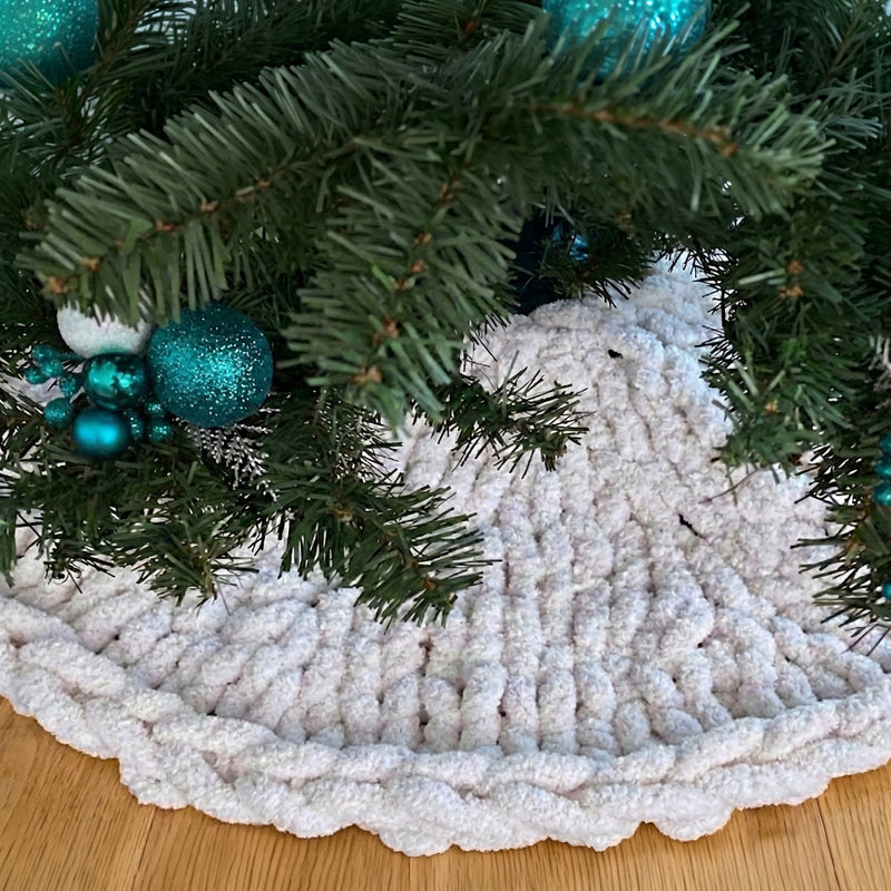 A close-up view of a Christmas tree with a white knitted tree skirt and blue ornaments.