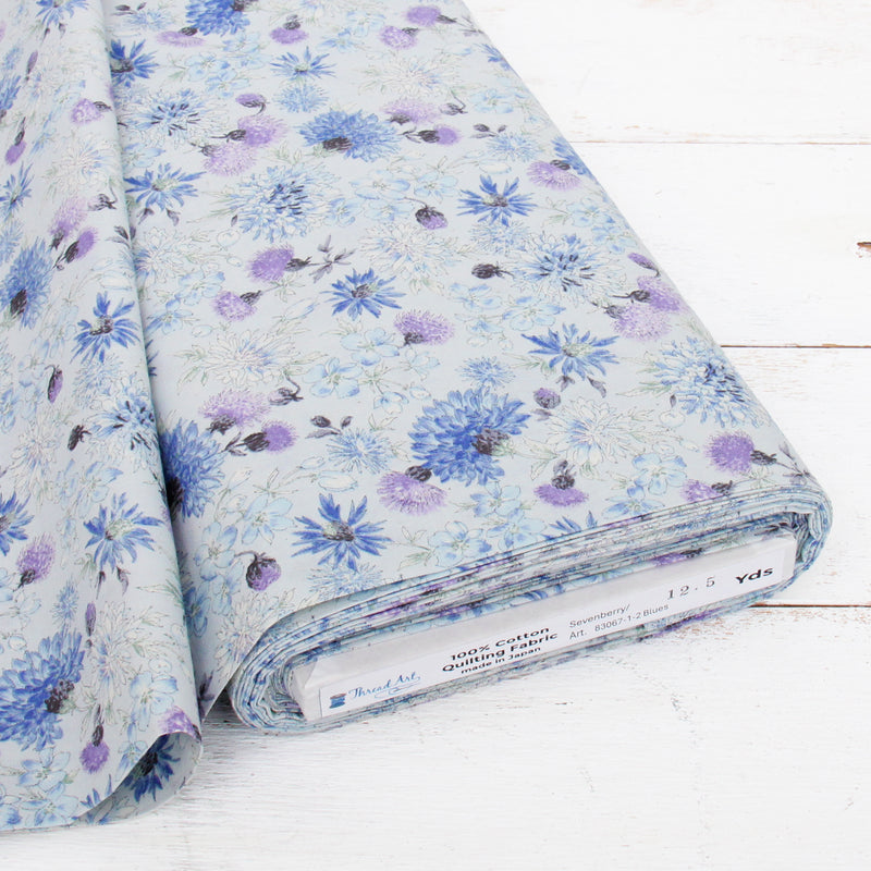 a piece of fabric with a floral pattern in shades of blue and purple. The fabric appears to be a quilted material, as indicated by the label on the bottom of the fabric.