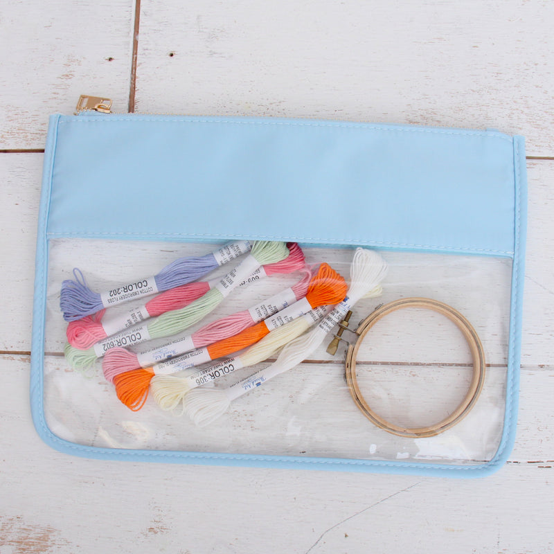 Light blue clear zipper pouch bag holding embroidery floss skeins and a wooden hoop