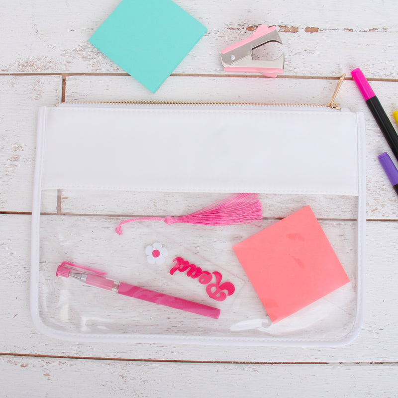 White clear zipper pouch bag with a pen, tassel, and sticky notes inside on a desk